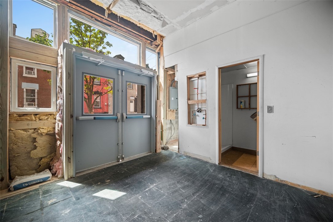 Unfinished interior with gray double doors, tall windows, exposed insulation, and an open doorway.