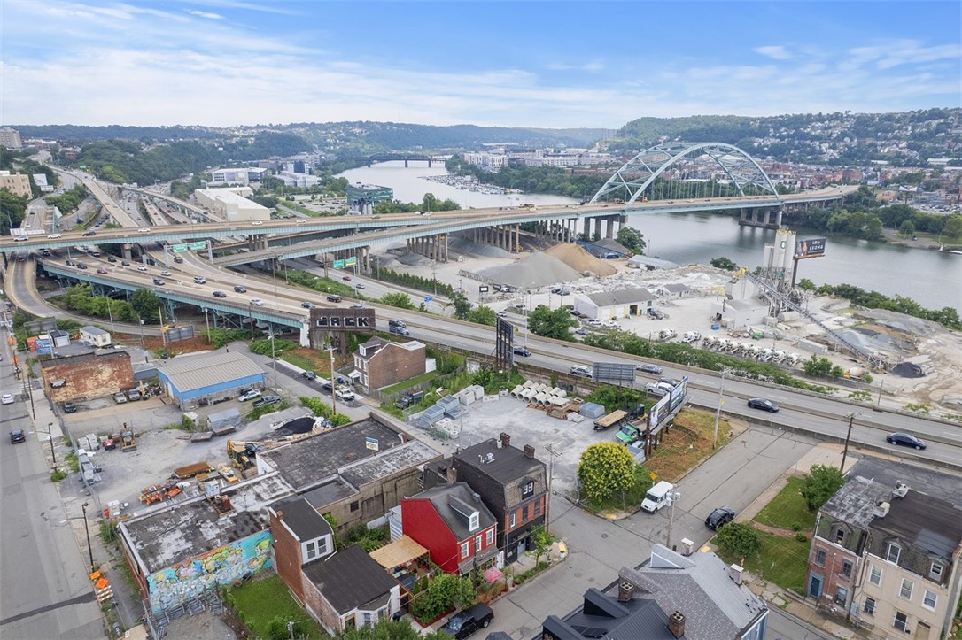 Aerial view of a Pittsburgh neighborhood with a river, steel arch bridge, and highway interchanges.