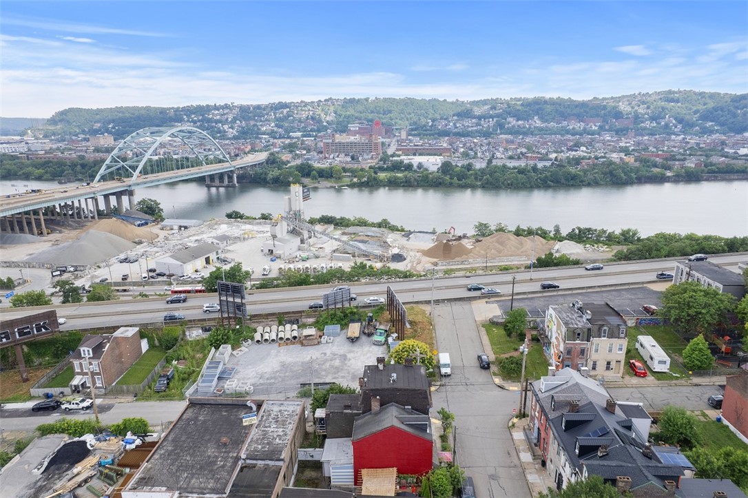 Aerial view of a river, arch bridge, and hillside neighborhood beyond nearby homes and streets.