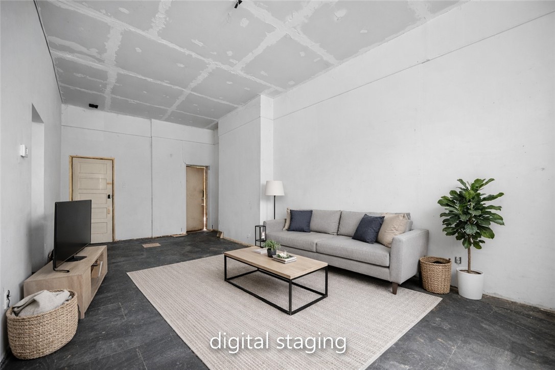 Digitally staged living room with a gray sofa, area rug, and unfinished ceiling.