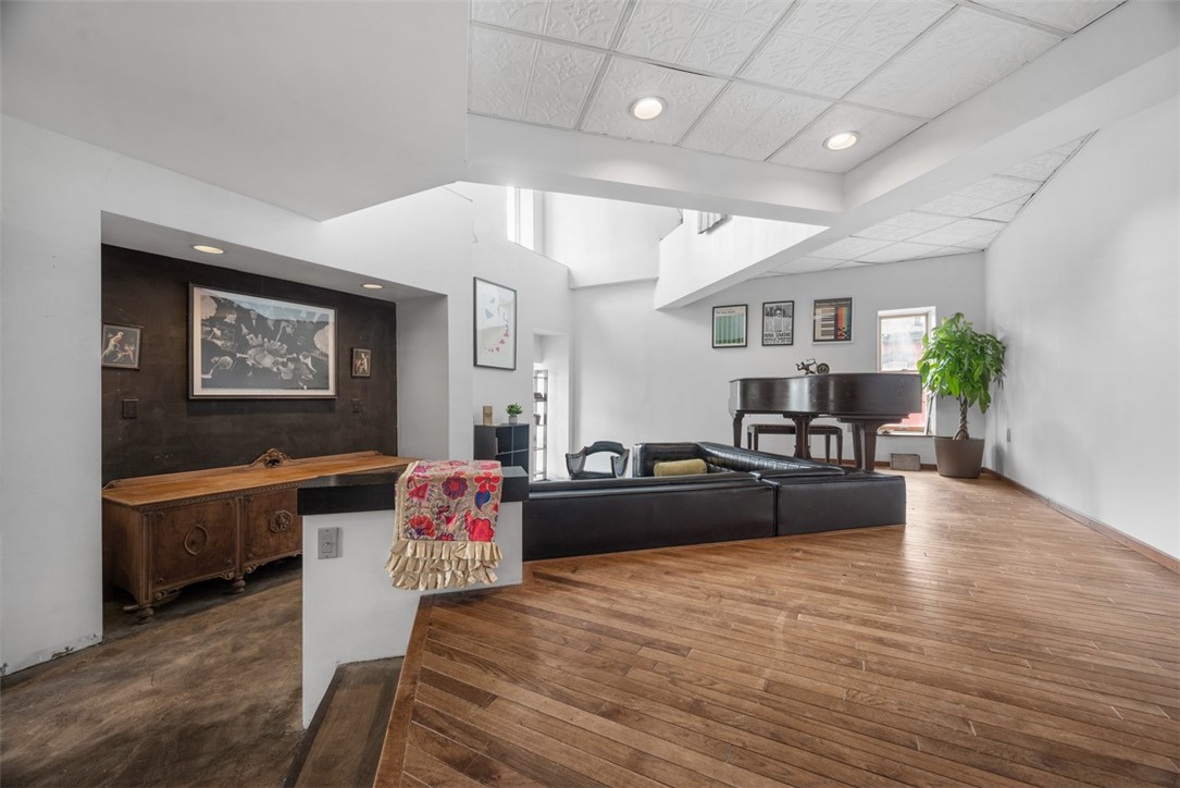 Furnished living room with a black leather sectional, grand piano, and warm wood floors.