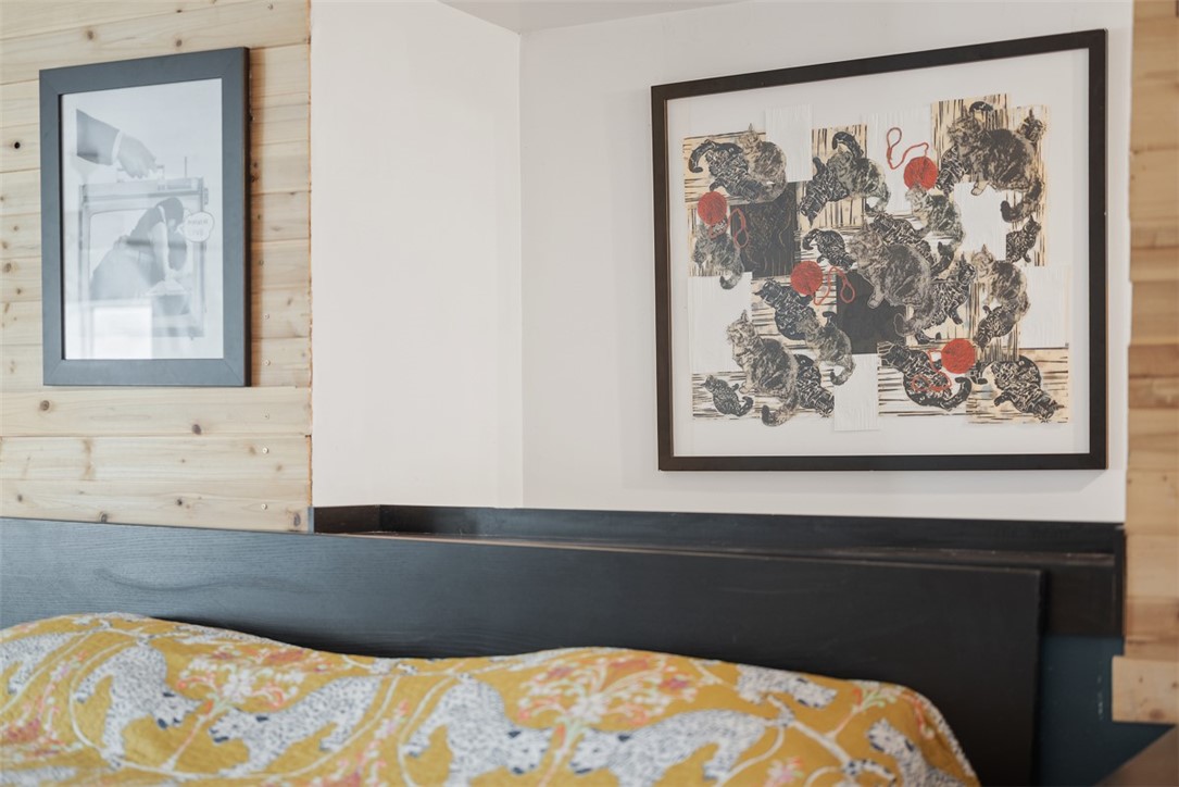 Bedroom with a patterned bedspread and framed artwork above a dark headboard.