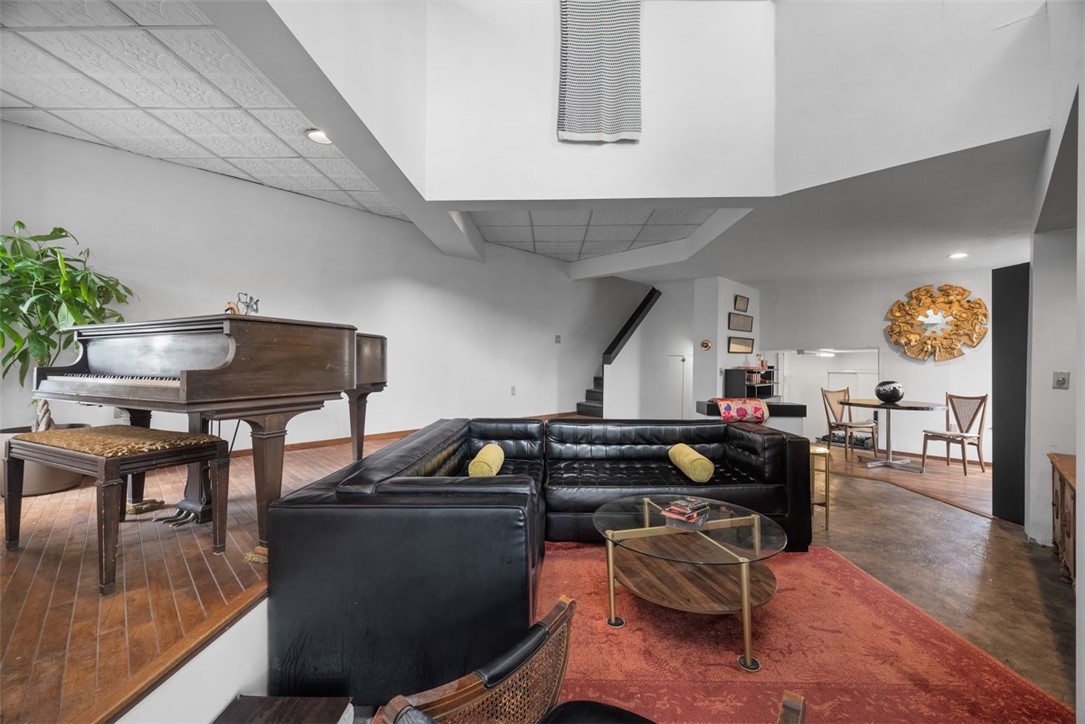 Living room with a black leather sectional, red rug, raised grand piano, and dining area.