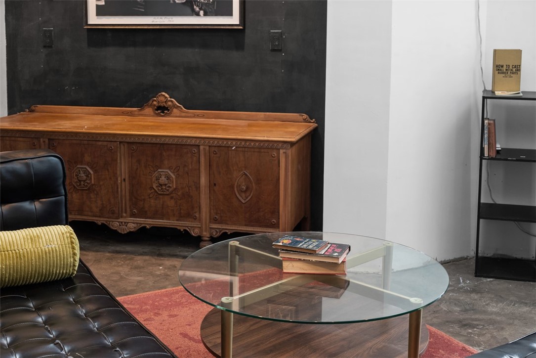 Living room with a black leather sofa, glass coffee table, ornate wooden sideboard, and red rug.