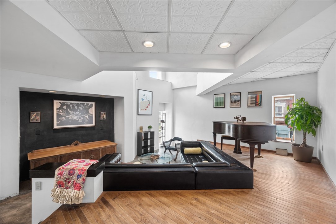 Living room with a black leather sectional, grand piano, and decorative pressed-tin ceiling.