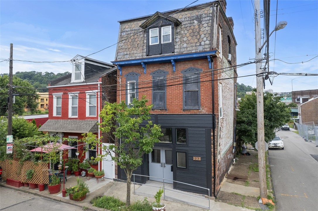 Narrow brick property with a shingled mansard roof, blue trim, and dark ground-floor facade.