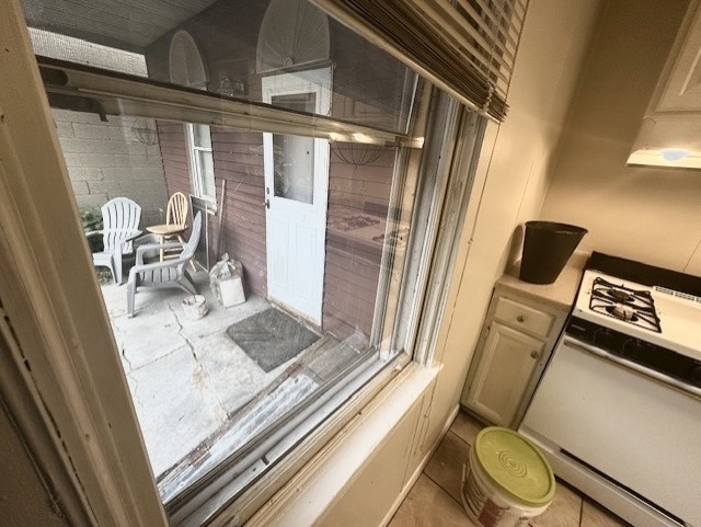Kitchen window overlooking a small patio with white chairs and a door, beside a gas range.