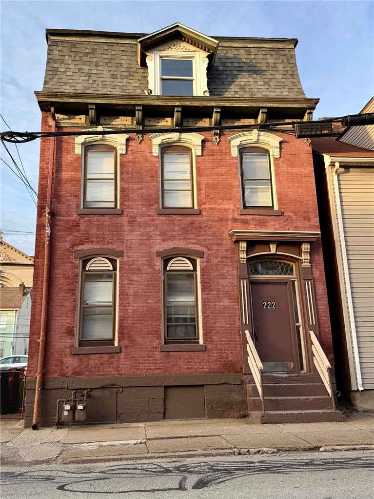 Red brick three-story house with a mansard roof, ornate cream window trim, and an entry marked 222.