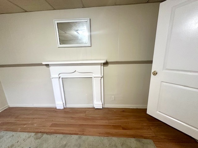 Vacant room with wood flooring, a white decorative mantel and mirror, and an open door.