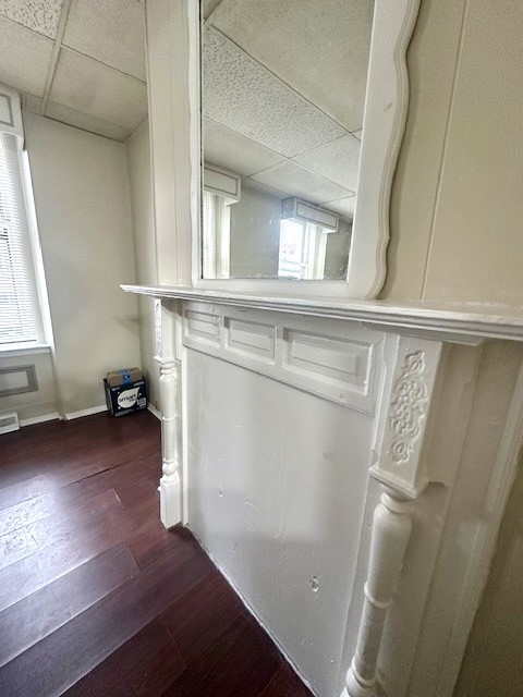 Room with an ornate white fireplace mantel, large mirror, dark hardwood floors, and tall windows.