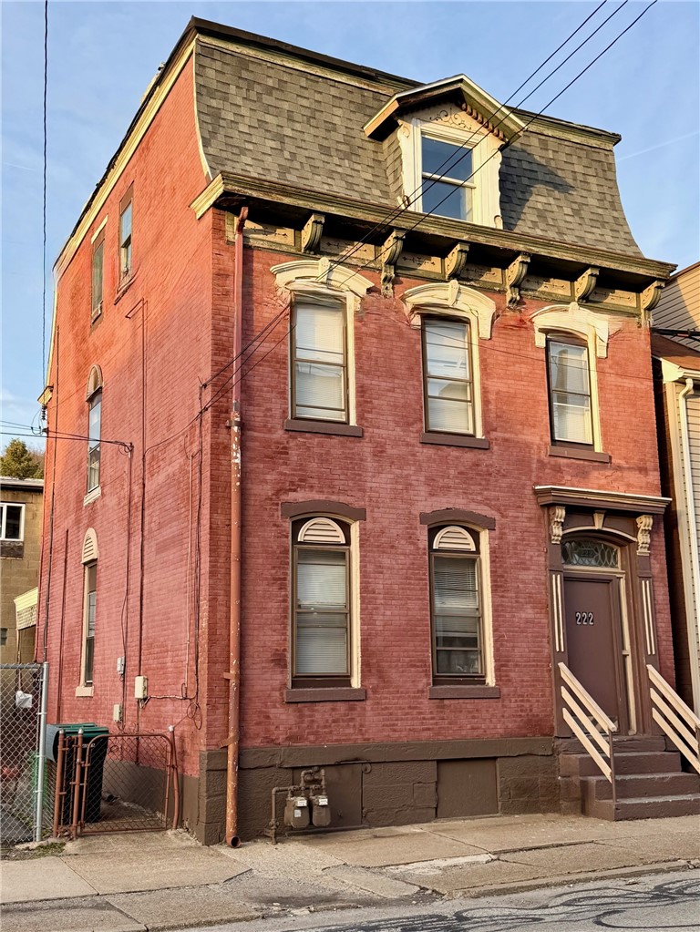 Red brick building with a mansard roof, ornate window trim, and raised entrance marked 222.