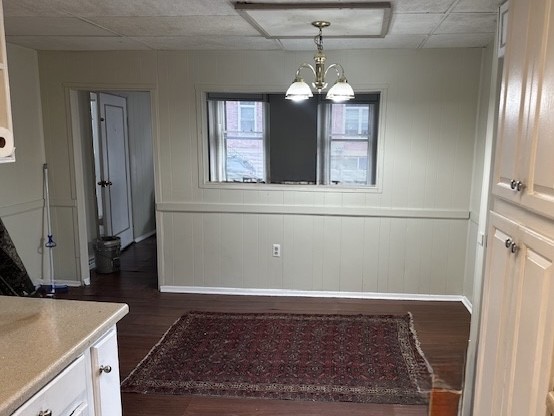 Dining area with dark wood floors, patterned rug, chandelier, and two windows.
