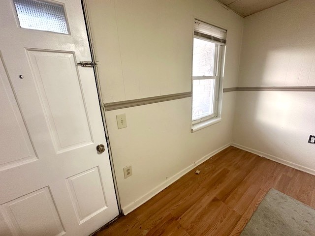 Empty room with hardwood floors, a white paneled door, and a window with a raised blind.