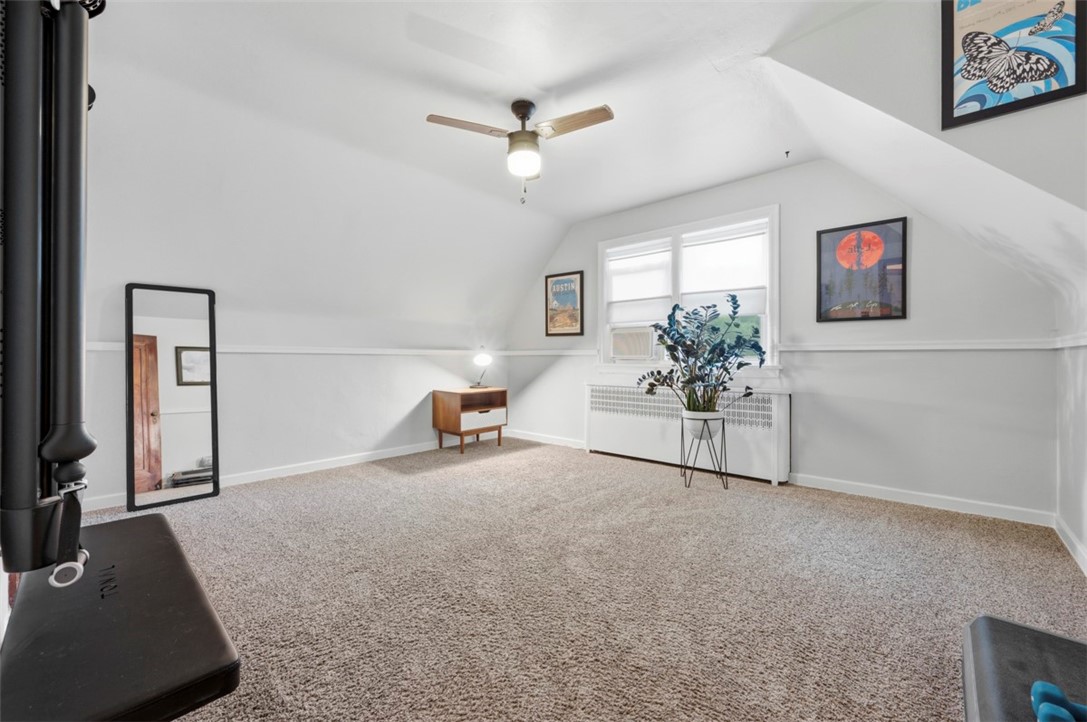 Carpeted attic room with sloped ceilings, a wood stove, and two bright windows.