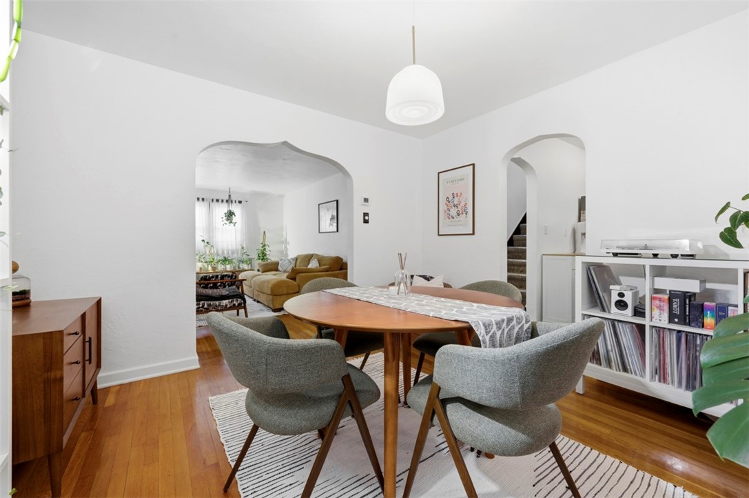 Dining room with a wooden table, gray chairs, hardwood floors, and arched openings to the living room.
