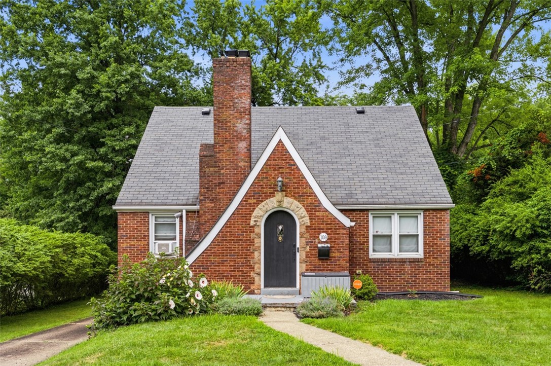 Red-brick house with an arched stone-framed entry, tall chimney, and leafy trees.