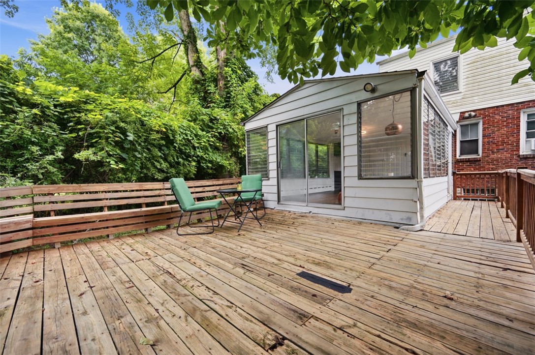 Wood deck beside an enclosed sunroom, with green chairs and dense trees along the railing.