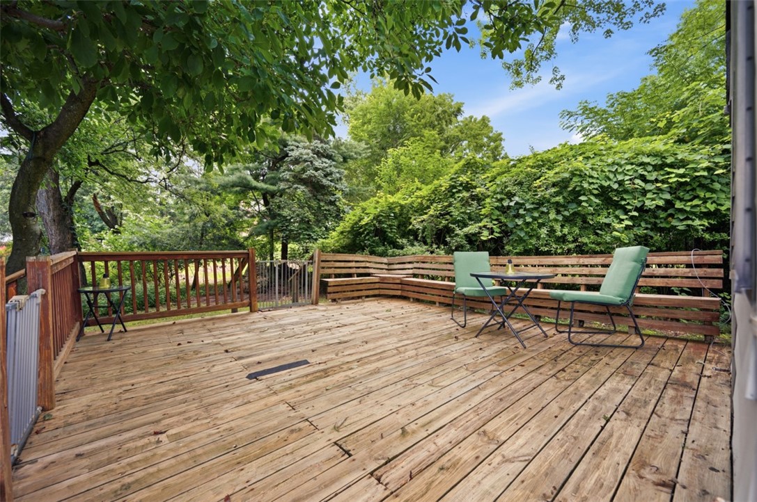 Wooden backyard deck with green chairs and table, surrounded by leafy trees.
