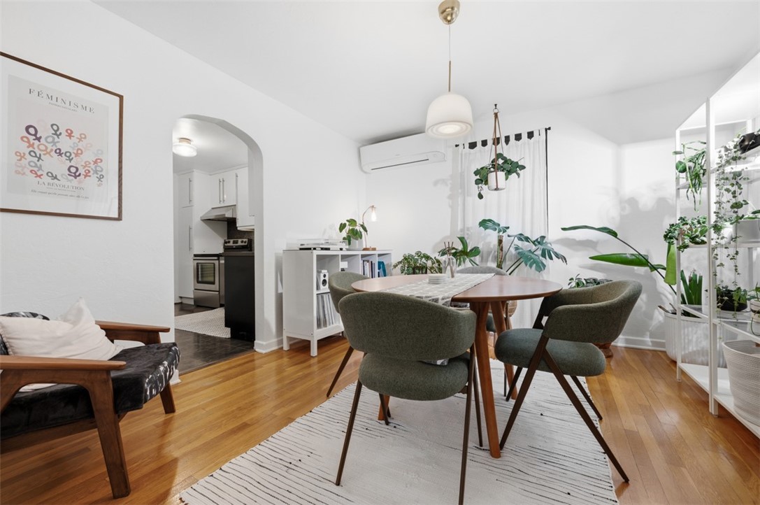 Dining area with green upholstered chairs, a wooden table, striped rug, and plants beside an arched kitchen opening.