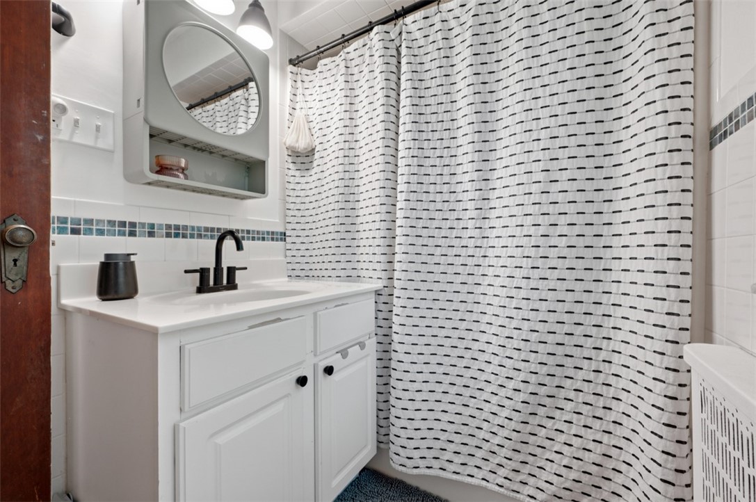 Bathroom with a white vanity, black faucet, patterned shower curtain, and blue-green accent tiles.