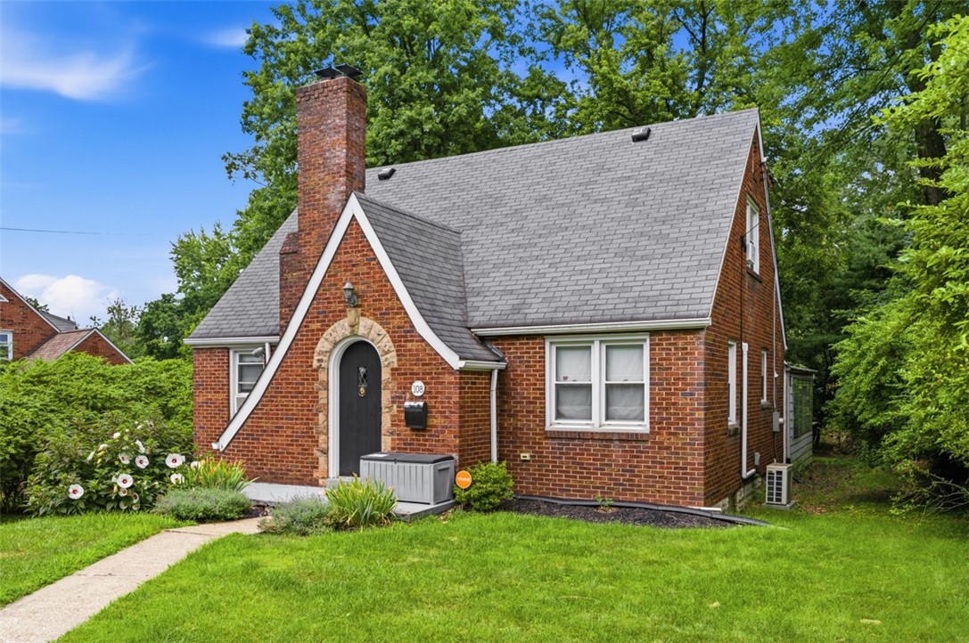 Brick house with a steep gray gabled roof, tall chimney, and arched front entry.