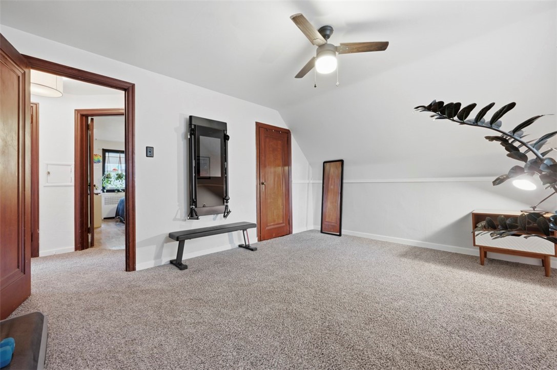 Carpeted bedroom with a sloped ceiling, ceiling fan, bench, and full-length mirror.