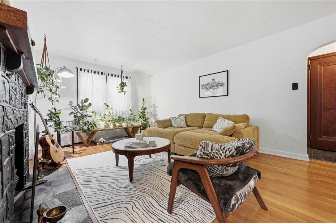 Living room with a mustard sofa, stone fireplace, patterned rug, and hardwood floors.