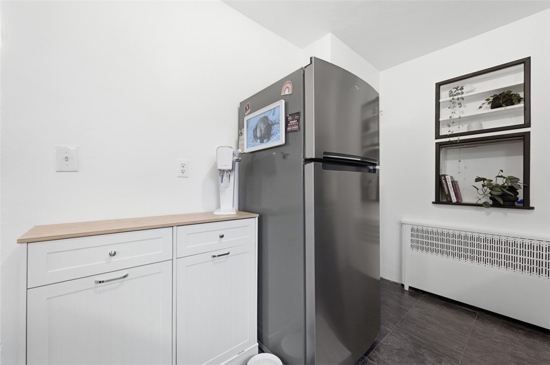 Compact kitchen with a stainless-steel refrigerator, white cabinetry, and recessed shelves with plants.