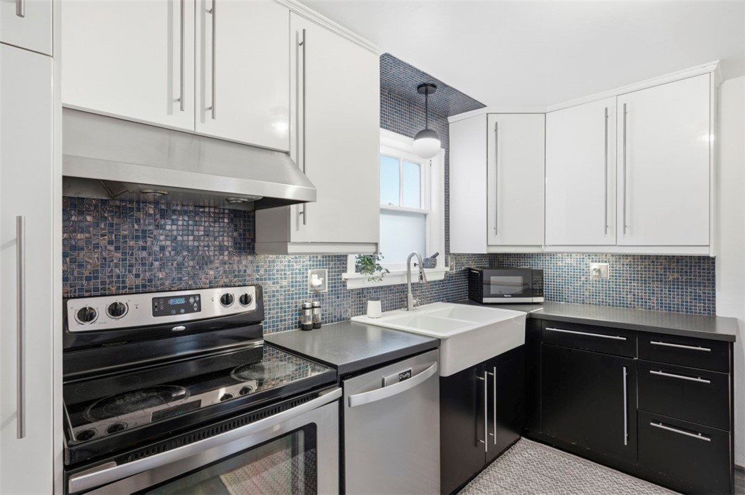 Kitchen with blue-gray mosaic tile, white upper cabinets, black lower cabinets, and a farmhouse sink.