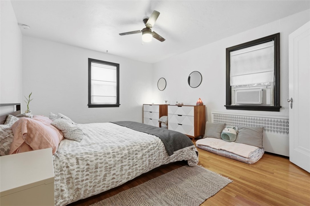 Furnished bedroom with patterned bedding, hardwood floors, and a cushioned pet bed beside the window.