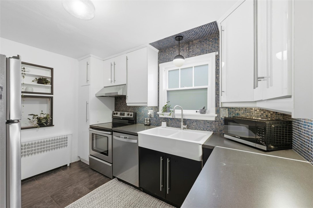 Renovated kitchen with farmhouse sink, stainless appliances, and blue-gray mosaic backsplash.