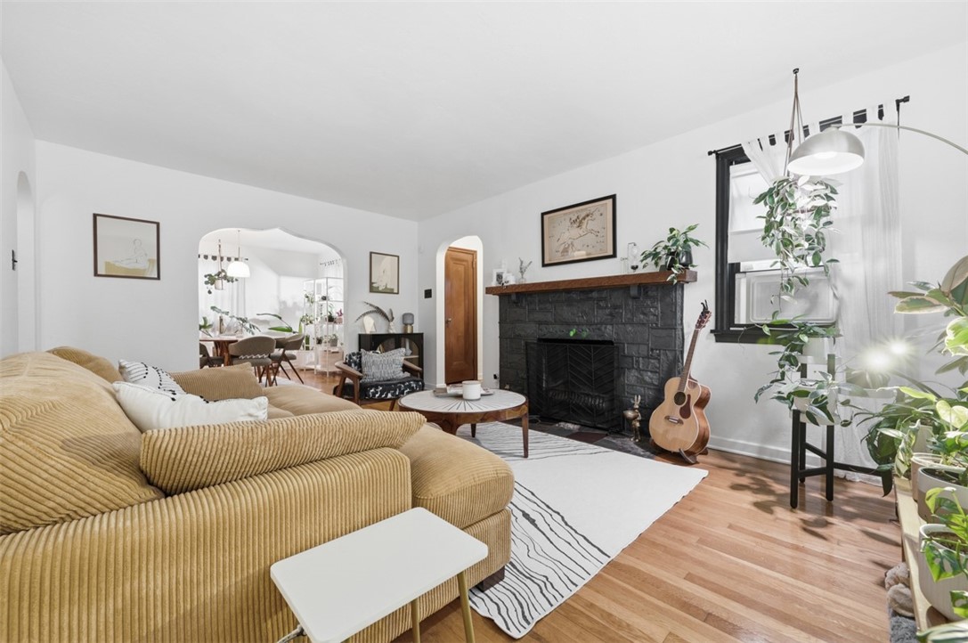 Living room with a tan sectional, stone fireplace, hardwood floors, and an arched opening to the dining area.
