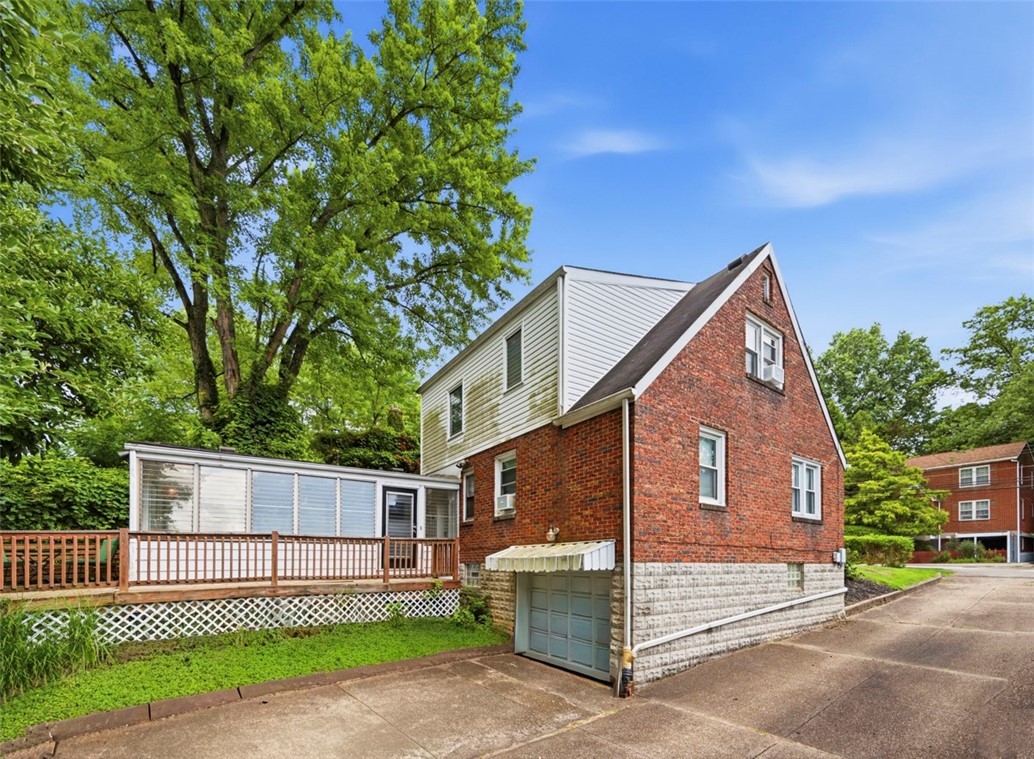 Red brick house with a white upper gable, raised deck, and driveway garage entrance.