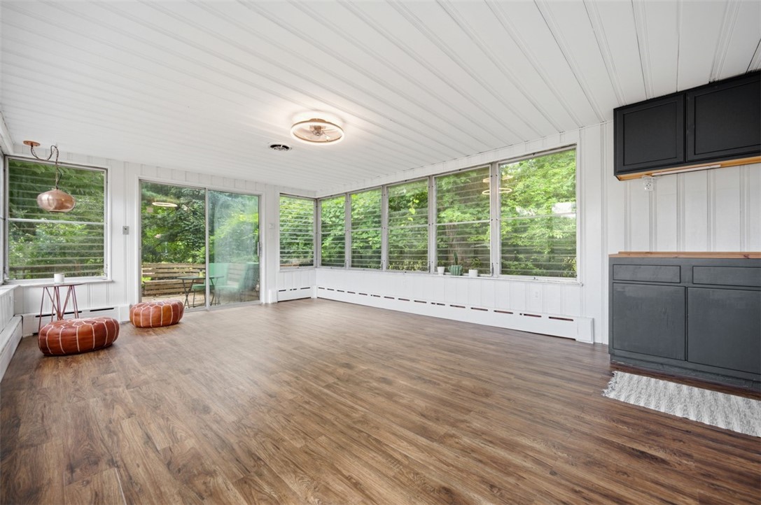 Enclosed sunroom with broad windows, wood-look flooring, dark built-in cabinets, and leafy views.