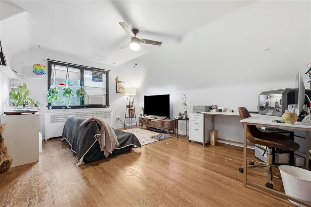 Furnished multipurpose room with hardwood floors, a desk, television, and window above a radiator.