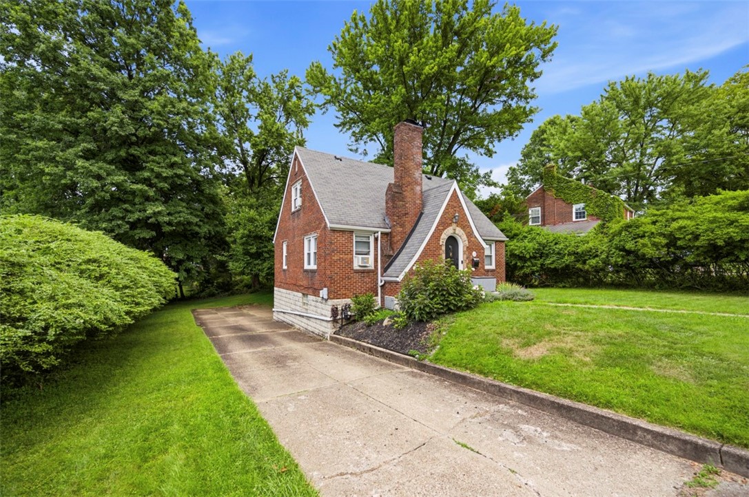 Red brick house with a tall chimney, steep gabled roof, and concrete driveway.