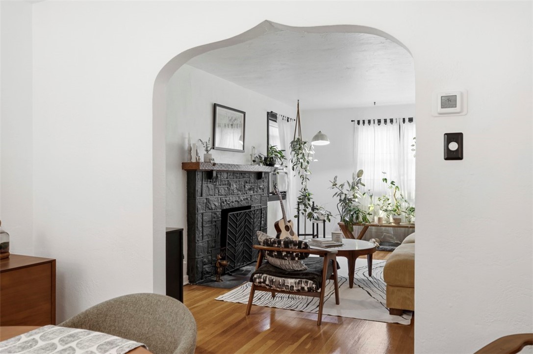 Living room with an arched entry, dark stone fireplace, hardwood floors, and plants by the windows.