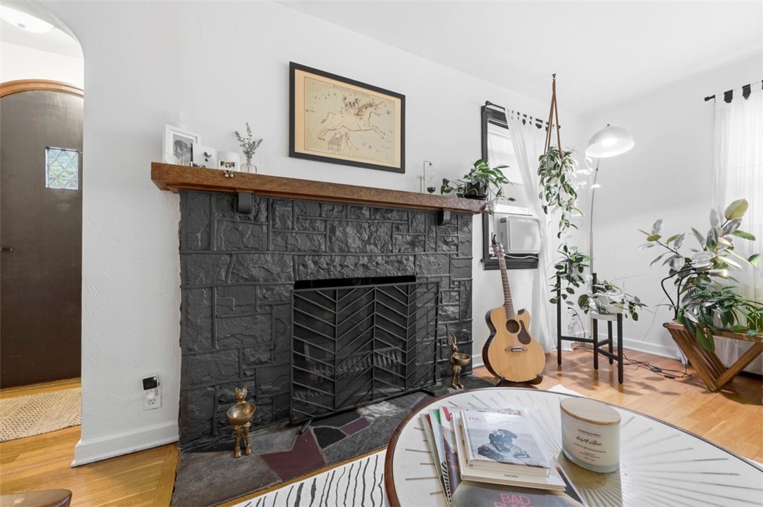 Living room with a dark stone fireplace, acoustic guitar, houseplants, and hardwood floors.