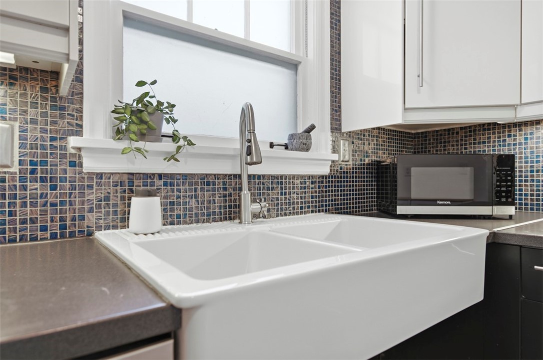 Kitchen with a white farmhouse sink, stainless-steel faucet, and blue mosaic tile backsplash.
