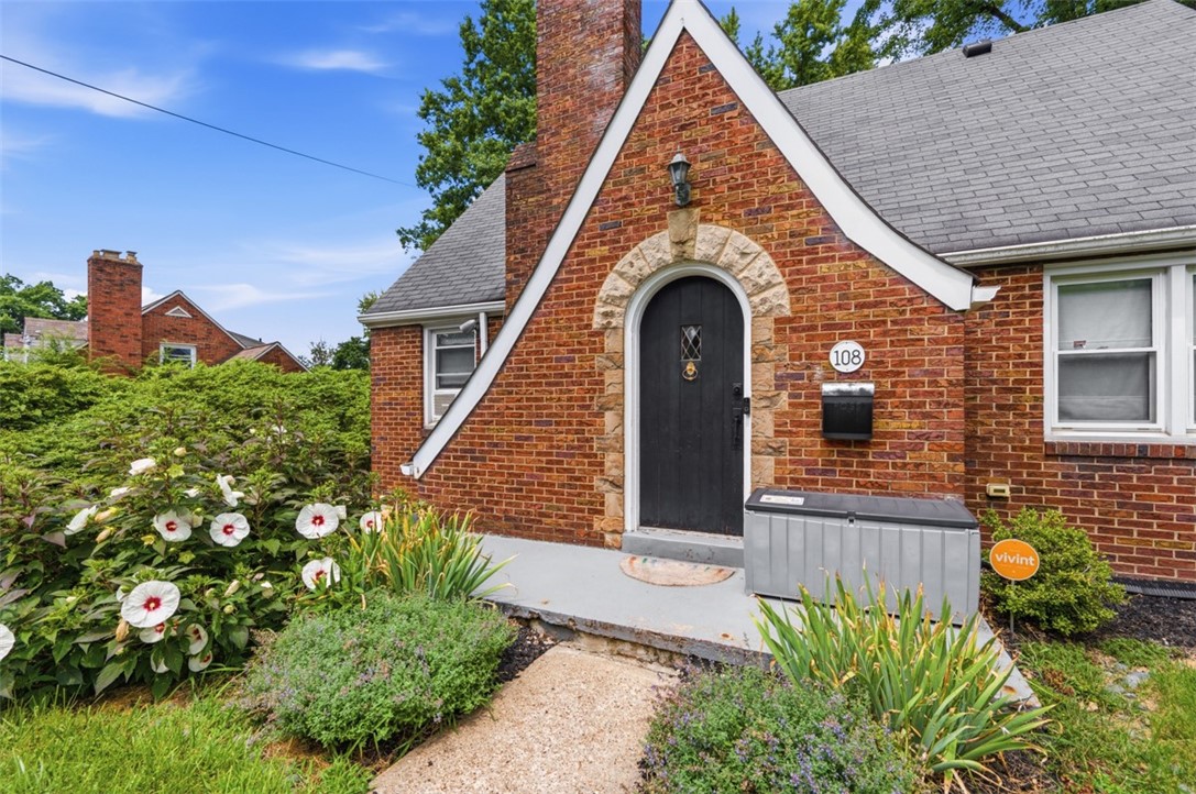 Brick home's arched black front door framed by stone trim, with flowering landscaping.