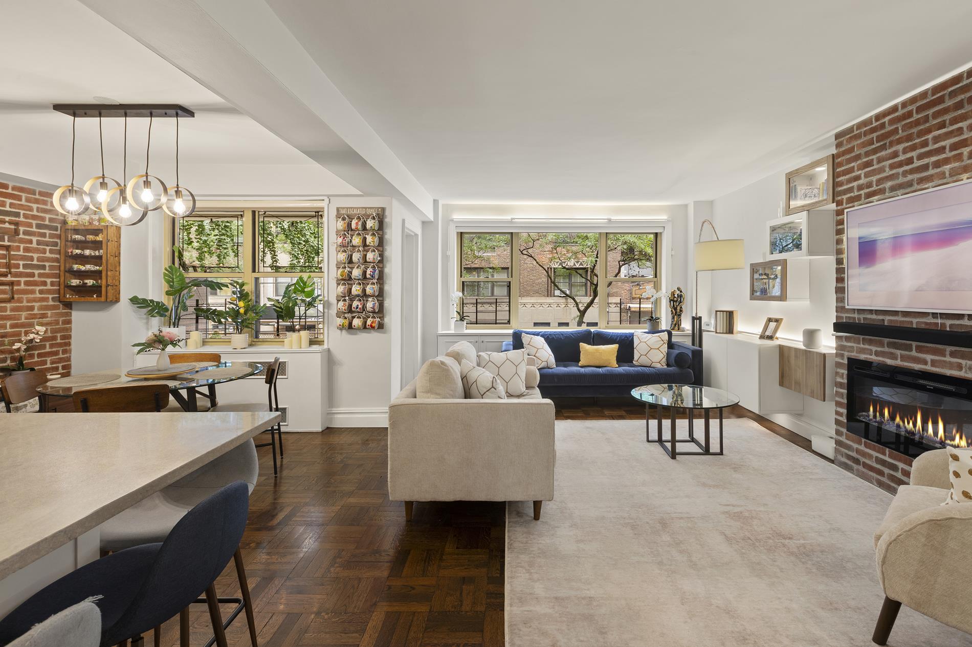 Open-plan living and dining room with exposed brick, parquet floors, and a modern fireplace.