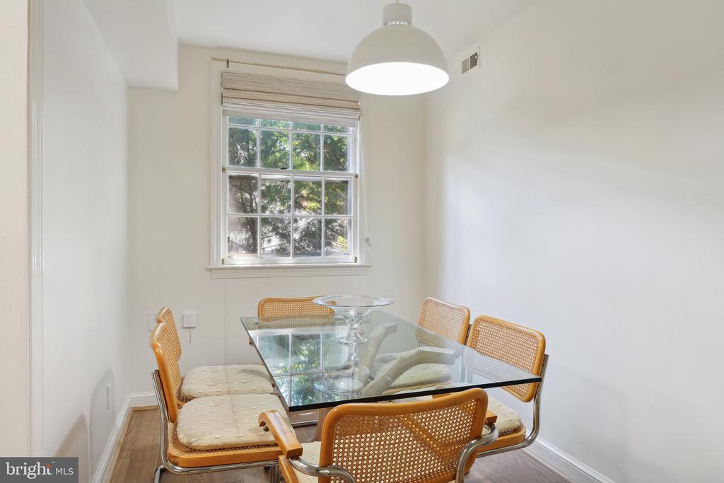 Dining room with a glass-top table, woven cane chairs, and a large window overlooking trees.