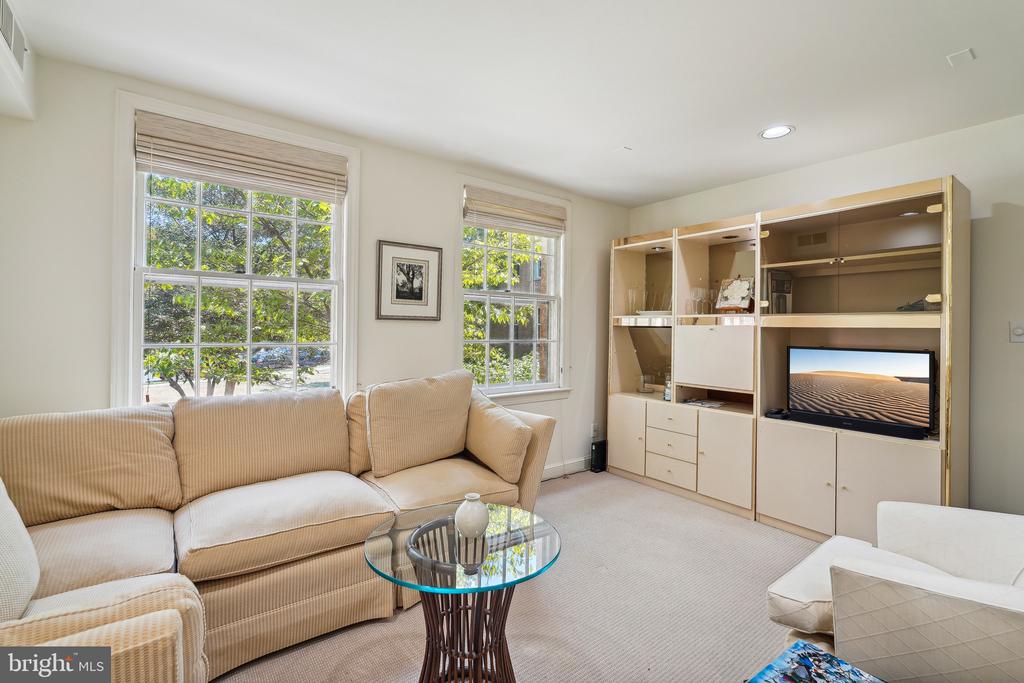 Living room with a beige sofa, glass coffee table, and built-in shelving beside two large windows.