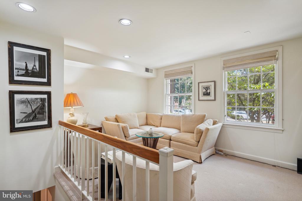 Living room with a beige sectional, glass coffee table, and large windows overlooking leafy trees.