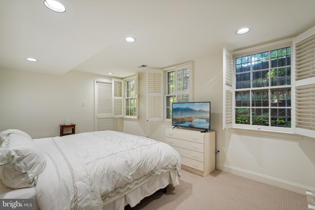 Bedroom with a white bed, shuttered windows, and a dresser topped with a television.