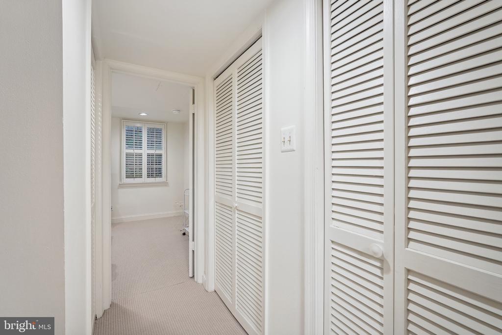 Bright hallway with louvered closet doors leading to a carpeted room with a shuttered window.