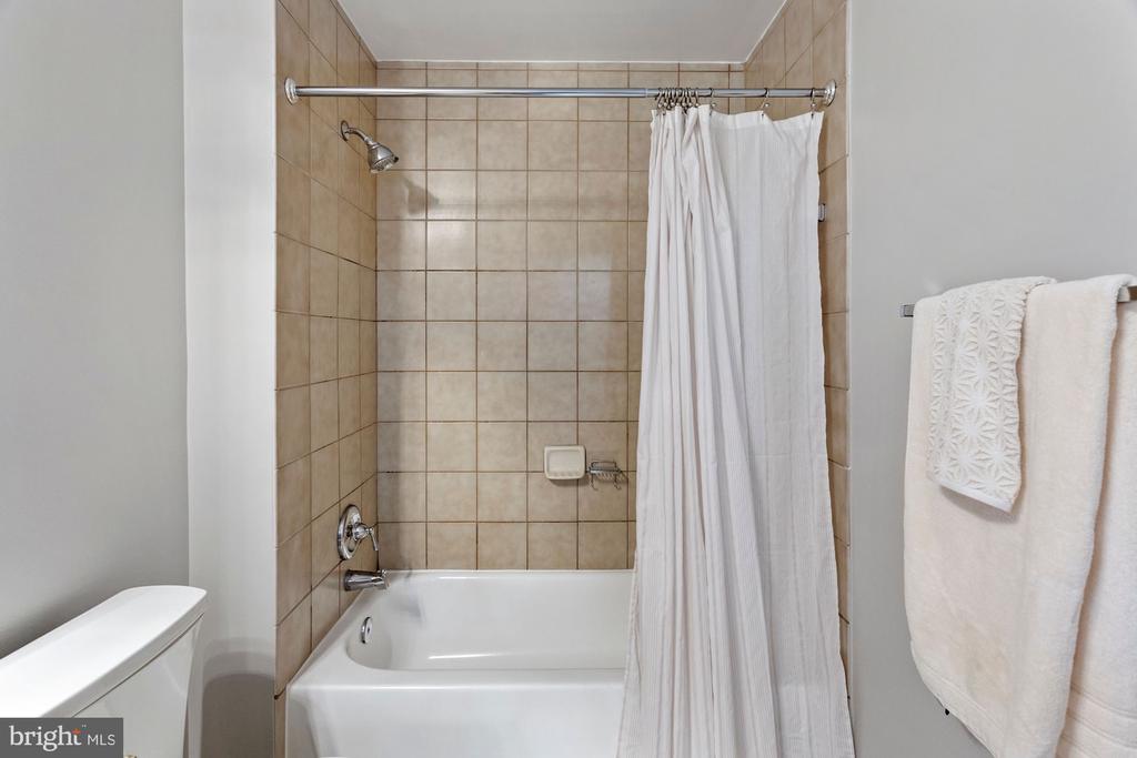 Bathroom with a white bathtub, tan tiled shower walls, and white towels.
