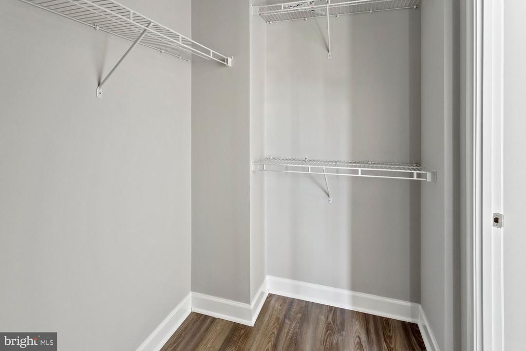 Empty walk-in closet with white wire shelving and wood-look flooring.