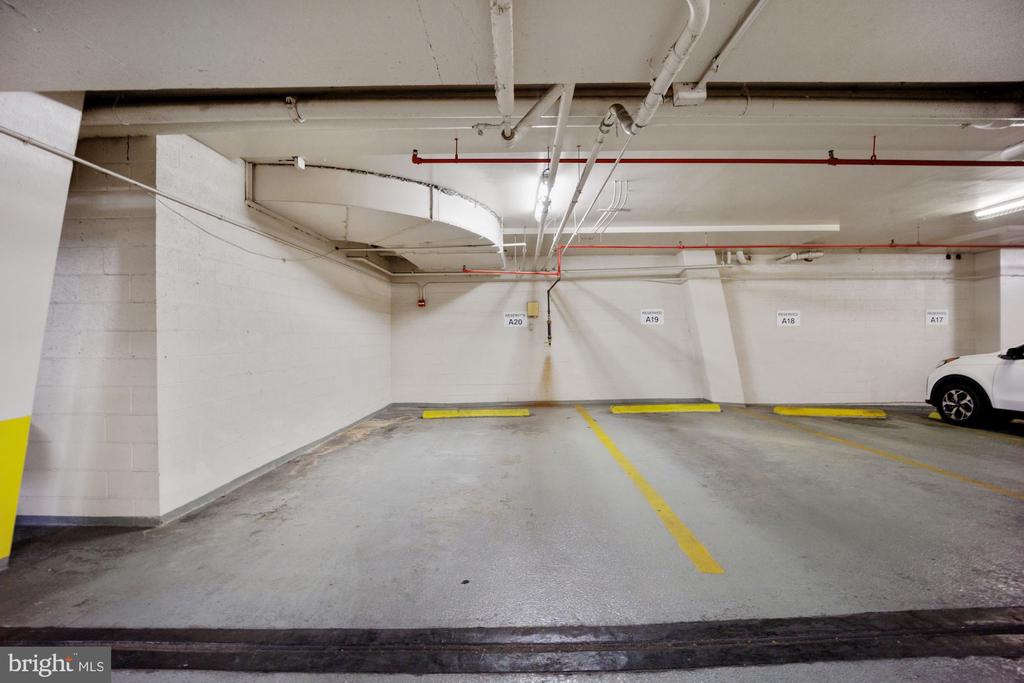Indoor parking garage with marked spaces, yellow wheel stops, and a white car at the edge.