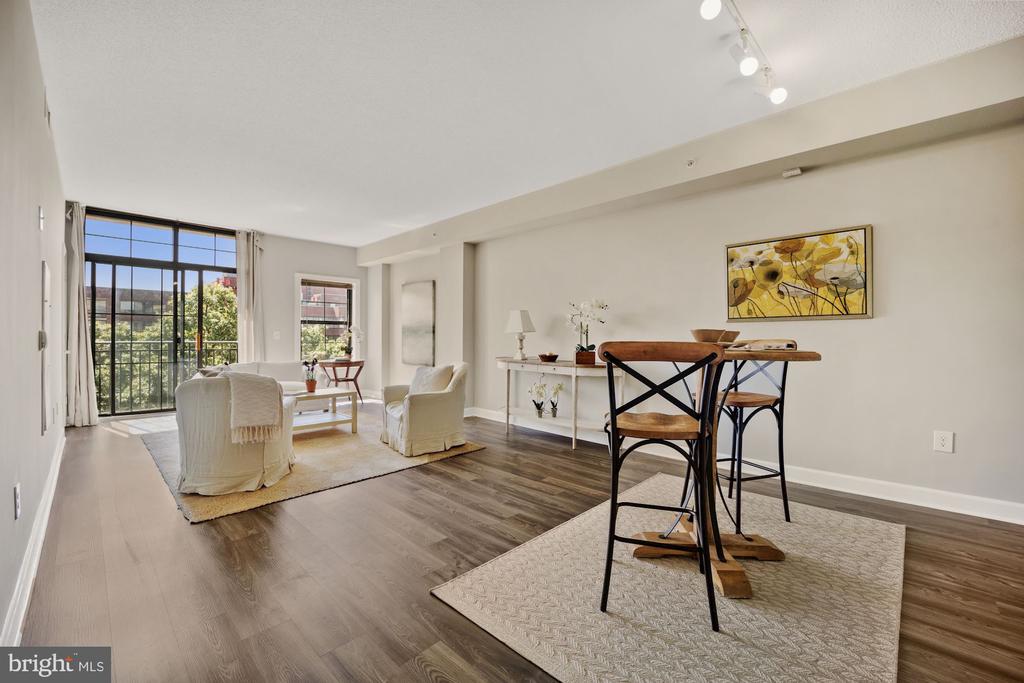 Open-plan living and dining area with light seating, dark wood floors, and a large window.